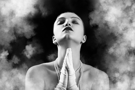 sensual luxury young woman with closed eyes in white gloves on black background with clouds prays, monochromeの写真素材