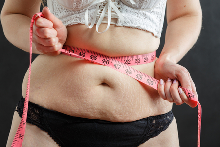 thick woman check her stomach fat with tapeの写真素材