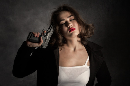 armed woman in black coat with closed eyes on dark backgroundの写真素材