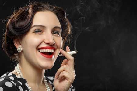 happy young woman smoking joint on black background, laughing