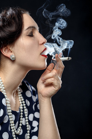 blond young woman smoking joint on black backgroundの写真素材