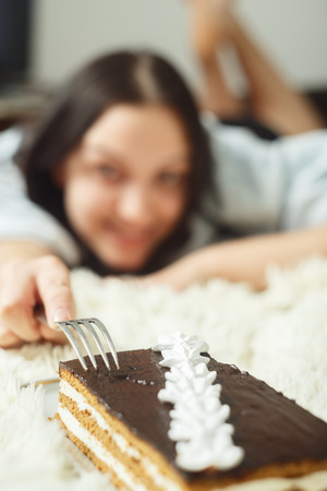 happy young woman with sweet cake lying on bed smilingの写真素材