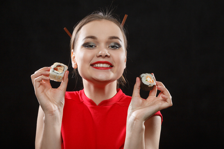 fun beautiful woman in red dress with sushi rolls on black background eating sushi smilingの写真素材