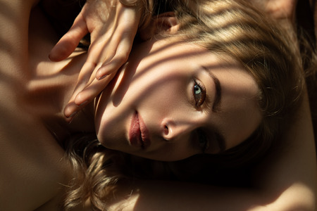 sensual beautiful woman lying in sunlight with blinds shadows, looking at cameraの写真素材
