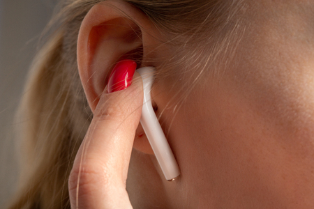 female ear with bluetooth earphone and finger closeupの写真素材