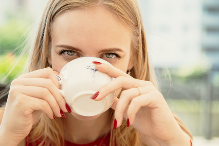 pretty young woman drinking tea in street cafe, looking at cameraの写真素材