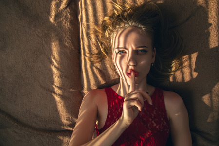 serious young woman lying, shows silence gesture looking at cameraの写真素材