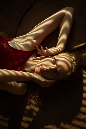 sensual girl lying on bed in sunlight with blinds shadowsの写真素材
