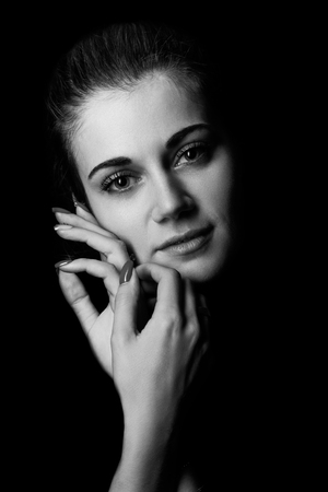pensive young woman in dark looking at camera smiling, monochromeの写真素材
