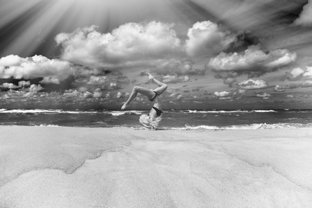 sports girl in a bathing suit in gymnastics pose on the seashore under sun rays, monochromeの写真素材