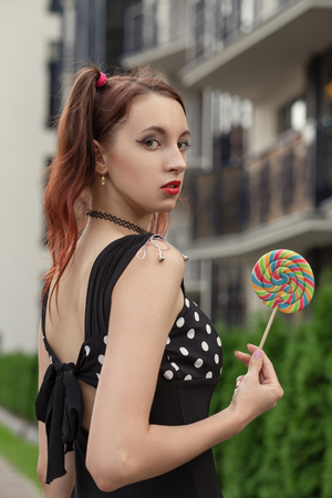 attractive young woman with lollipop in black dress posing on streetの写真素材