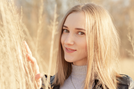 beautiful blond young woman at dry grass looking at camera, smilingの写真素材