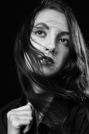 sad pensive young woman with flying hair on black background looking up thinkingの写真素材