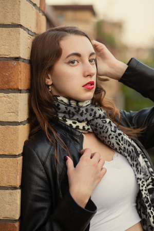 attractive sad young woman in leather coat near bricks wallの写真素材