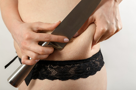 cutting with knife oversized female stomach side fat on white background isolatedの写真素材