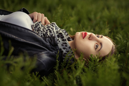 attractive sad young woman in leather coat lying on green grassの写真素材