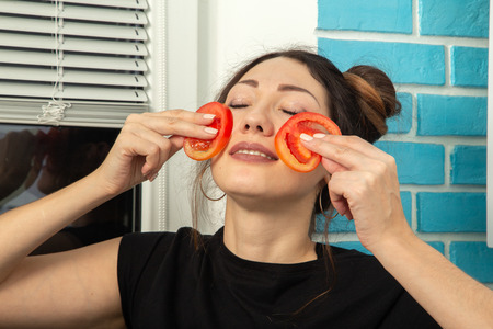 young woman puts tomato slices to the cheeksの写真素材