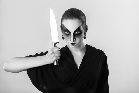 serious woman, professional geisha makeup, in black kimono with big kitchen knife looking at camera, monochromeの写真素材