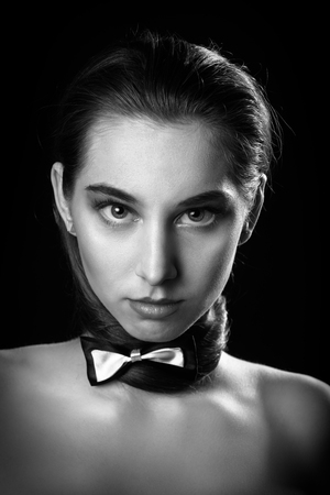 serious young woman with tie butterfly and bare shoulders on black background looking at camera, monochromeの写真素材