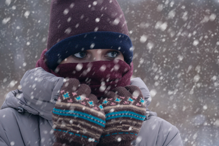 freezing young woman on winter meadow under falling snowの写真素材