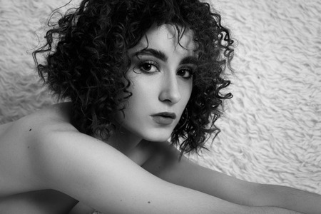 sensual nude curly young woman lying on white fur looking at camera, monochromeの写真素材