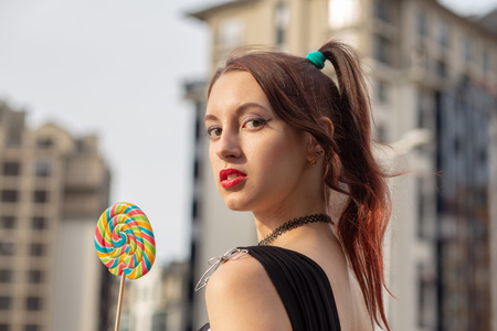 attractive young woman with lollipop in black dress posing on streetの写真素材