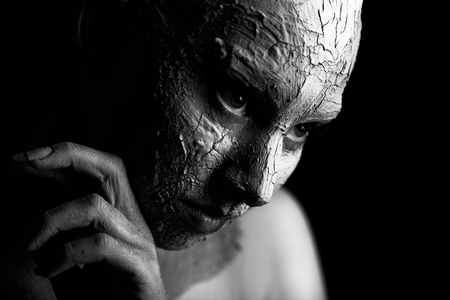 sad pensive woman with cracked cosmetic clay looking down on black background, monochromeの写真素材