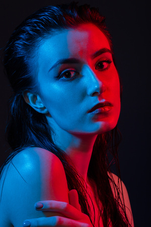 serious young woman in multicolor lights on black background looking at cameraの写真素材