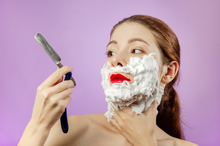 fun young woman has shave with open razor on violet background, looking at razorの写真素材