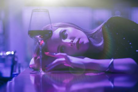 single luxury beautiful woman sitting with wine near bar in restaurant, ultraviolet toned imageの写真素材