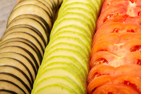 sliced tomatoes, zucchini and eggplant with knife on wooden desk top viewの写真素材