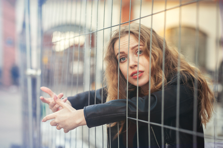 sad blond girl behind bars looking at cameraの写真素材