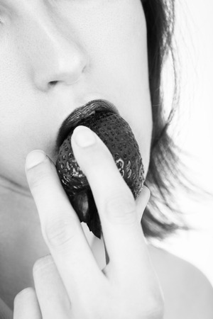 young sensual woman eats juicy strawberry on white background closeup view, monochromeの写真素材