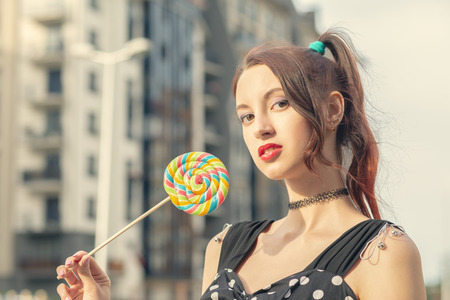 attractive young woman with lollipop in black dress posing on streetの写真素材