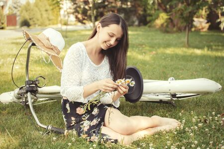 pretty girl with long brunette hair making wreath with camomilesの写真素材