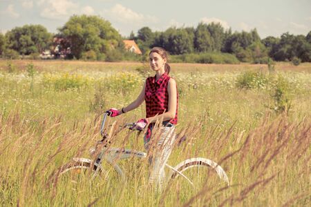 happy young woman walking with bike at at sunny meadowの写真素材