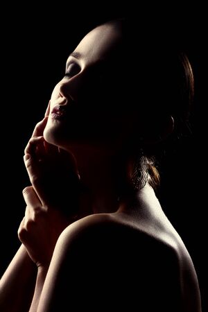 young topless sensual woman with closed eyes on black background, hands on chinの写真素材