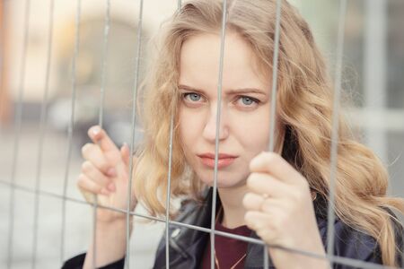 sad blond girl behind bars looking at camera