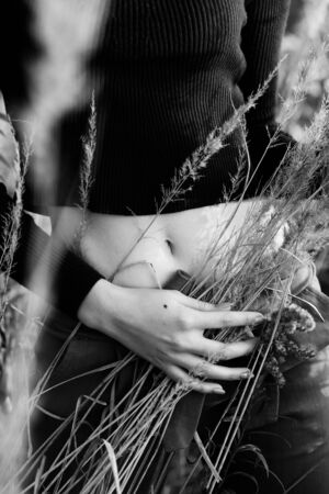 woman with slim body in dry grass front view closeup bare stomach, monochromeの写真素材