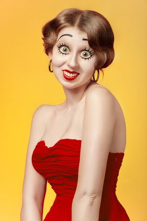 fun young woman with vintage pinup makeup making dolly face looking at camera, yellow backgroundの写真素材