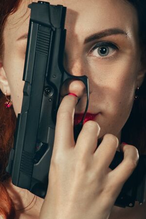 young woman cover her face with gun looking at camera closeup portrait