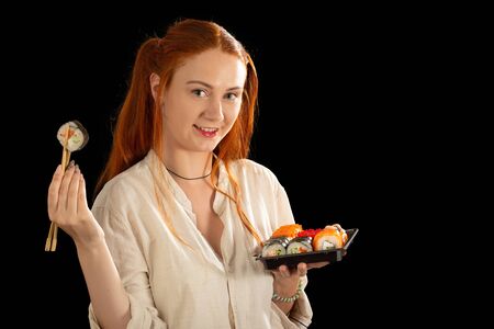 happy red hair young woman shows sushi on black background looking at cameraの写真素材