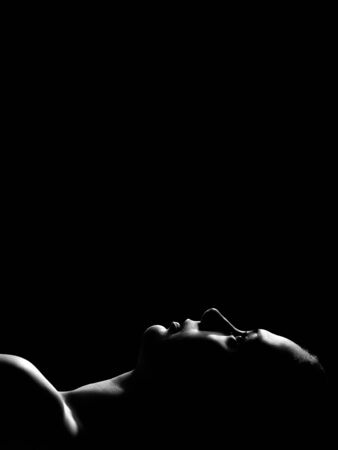 young pensive woman lying on black background with copy space, monochrome, profile viewの写真素材