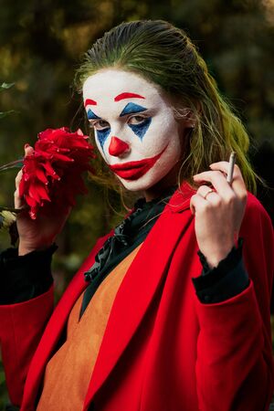 young woman with Joker makeup and costume looking at camera, smoking