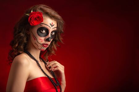 young woman with santa muerte makeup on red background with copy space looking at camera