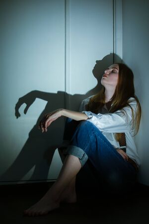 sad young woman sitting in dark in corner looking up