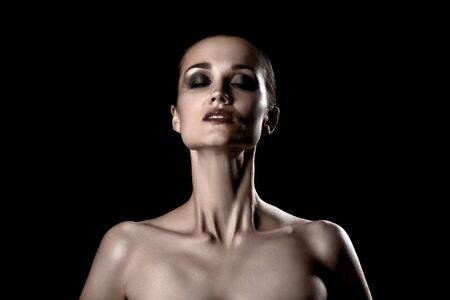 beautiful young woman with luxury makeup and bare shoulders hold face up, closed eyes on black backgroundの写真素材