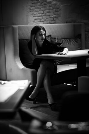 single luxury beautiful woman with wine sitting in restaurant looking aside, monochromeの写真素材