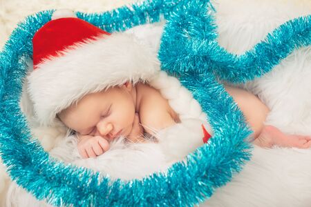 cute newborn girl in christmas cap sleeping on white fur