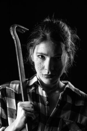 serious young bloody woman with crowbar in dark looking at camera monochrome imageの写真素材